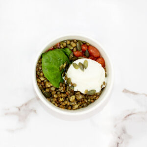 Une petite salade d’haricots fagioli, lentilles, pousses d’épinards, œuf poché et graines de courge dans un bol en carton sur un fond de marbre blanc